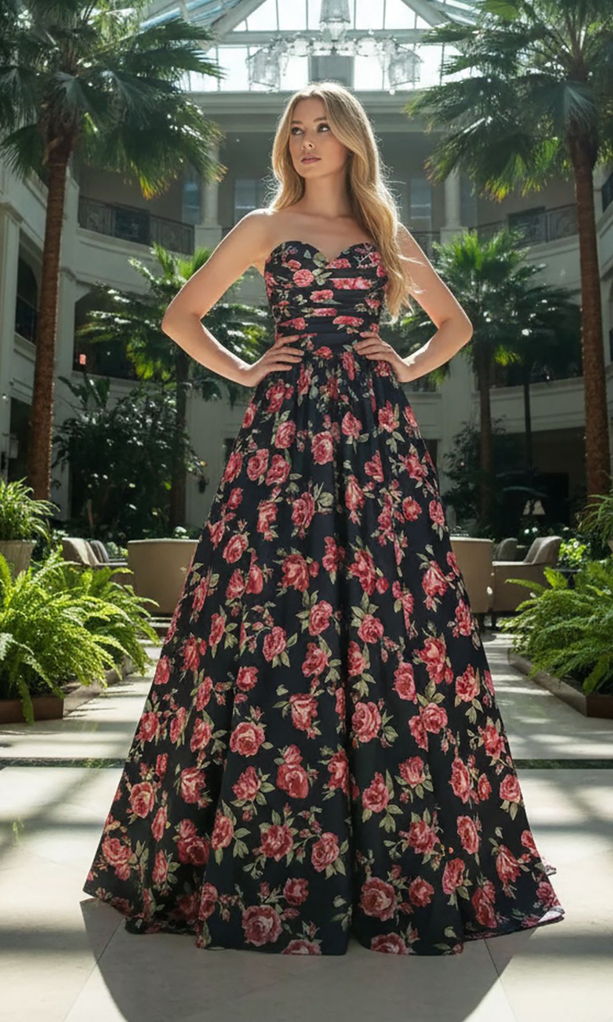 A woman stands in a sunlit indoor garden wearing the Amelia Couture 8070 long black prom dress, featuring a strapless design, romantic lace-up back, and elegant floor-length silhouette.